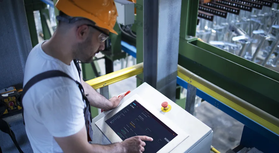 An engineer in a hard hat operating a touchscreen control panel on a factory floor